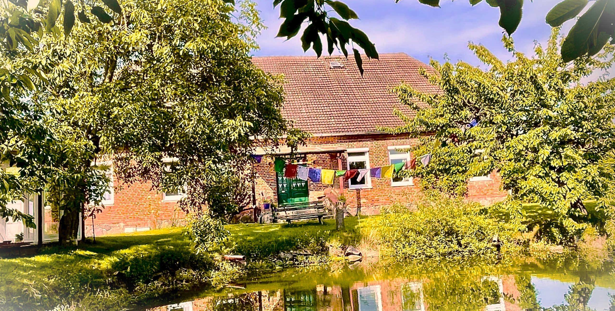 The Historic Parsonage with colourful prayer flags strung across the entrance, reflected in the pond